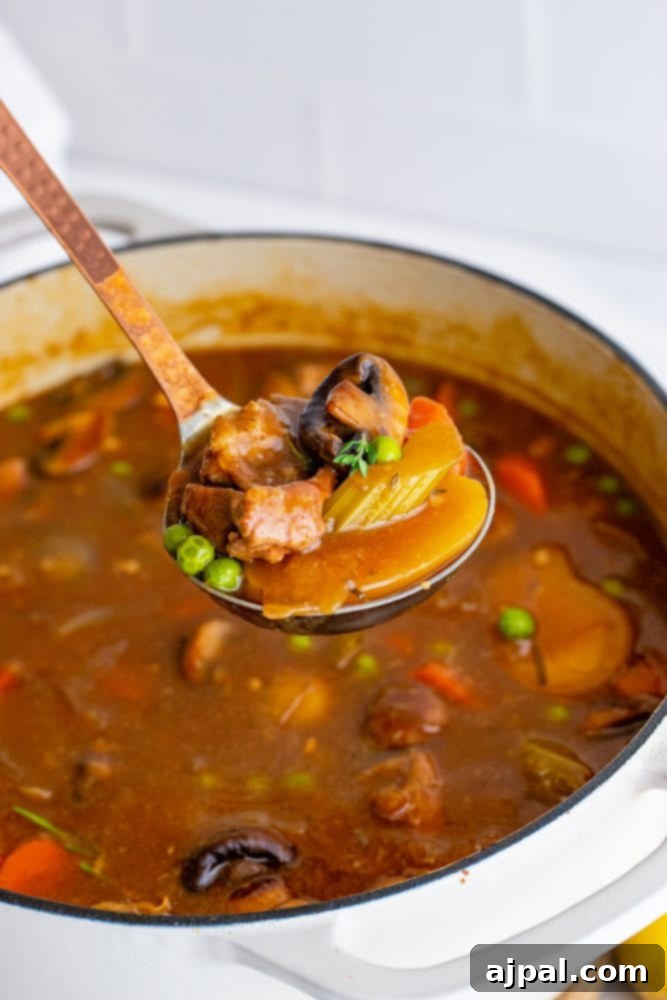 A spoon scooping a generous portion of venison stew from a Dutch oven, highlighting the tender meat and vegetables.