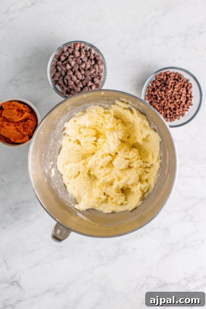 A bowl containing a creamy mixture of cookie dough ingredients, ready for the addition of pumpkin puree.
