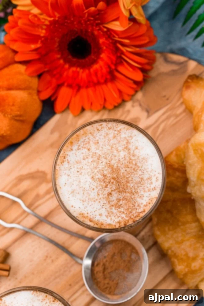 A stunning close-up of a homemade pumpkin spice latte, beautifully presented on a wooden cutting board with a scattering of cinnamon and whole star anise.