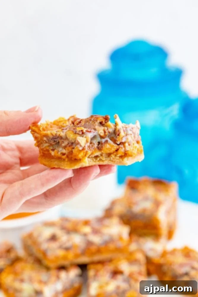 A hand holding up a single piece of pumpkin magic bar, showcasing its layers and delicious texture