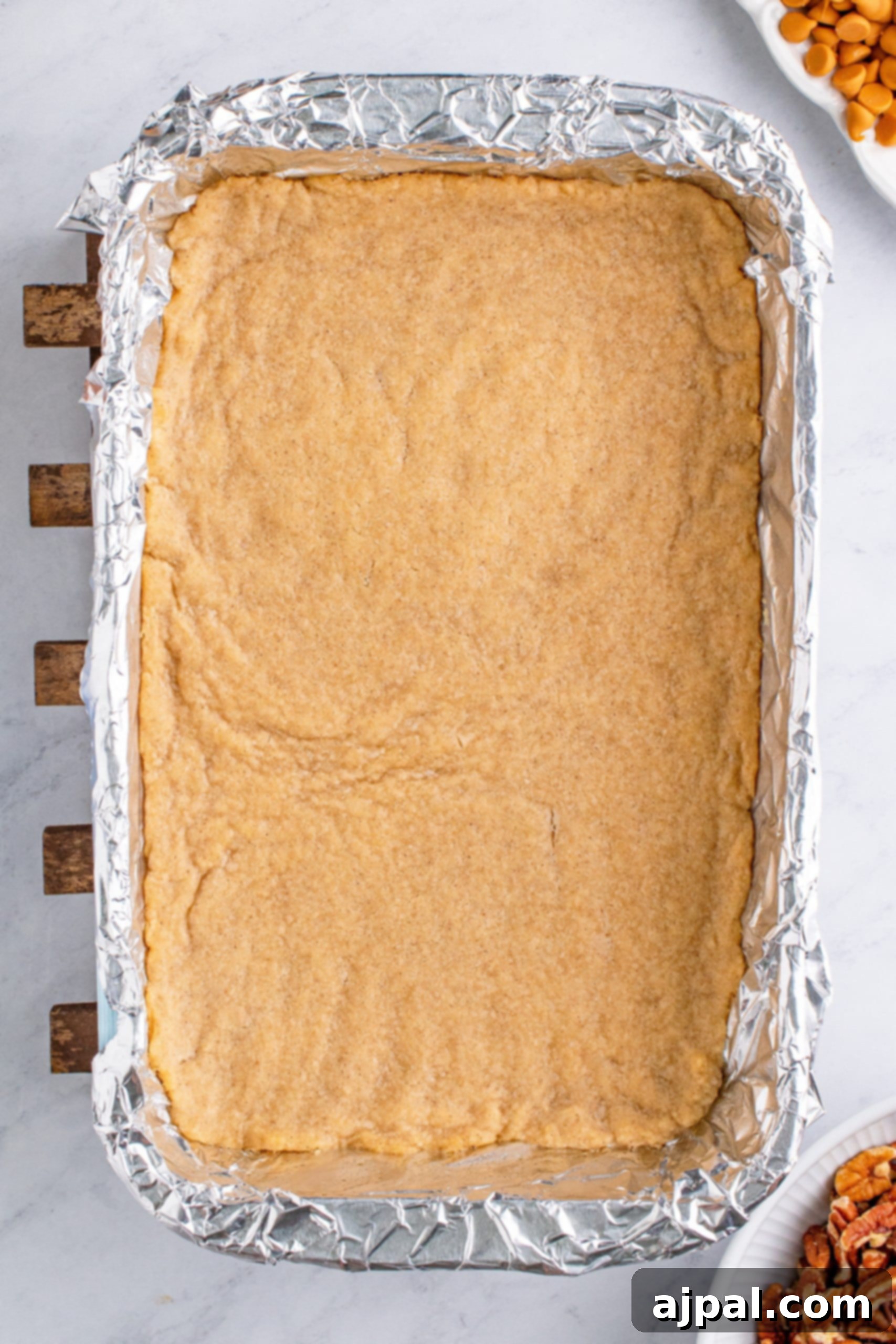 Baked cookie dough forming the base in a foil-lined pan, ready for the next layer