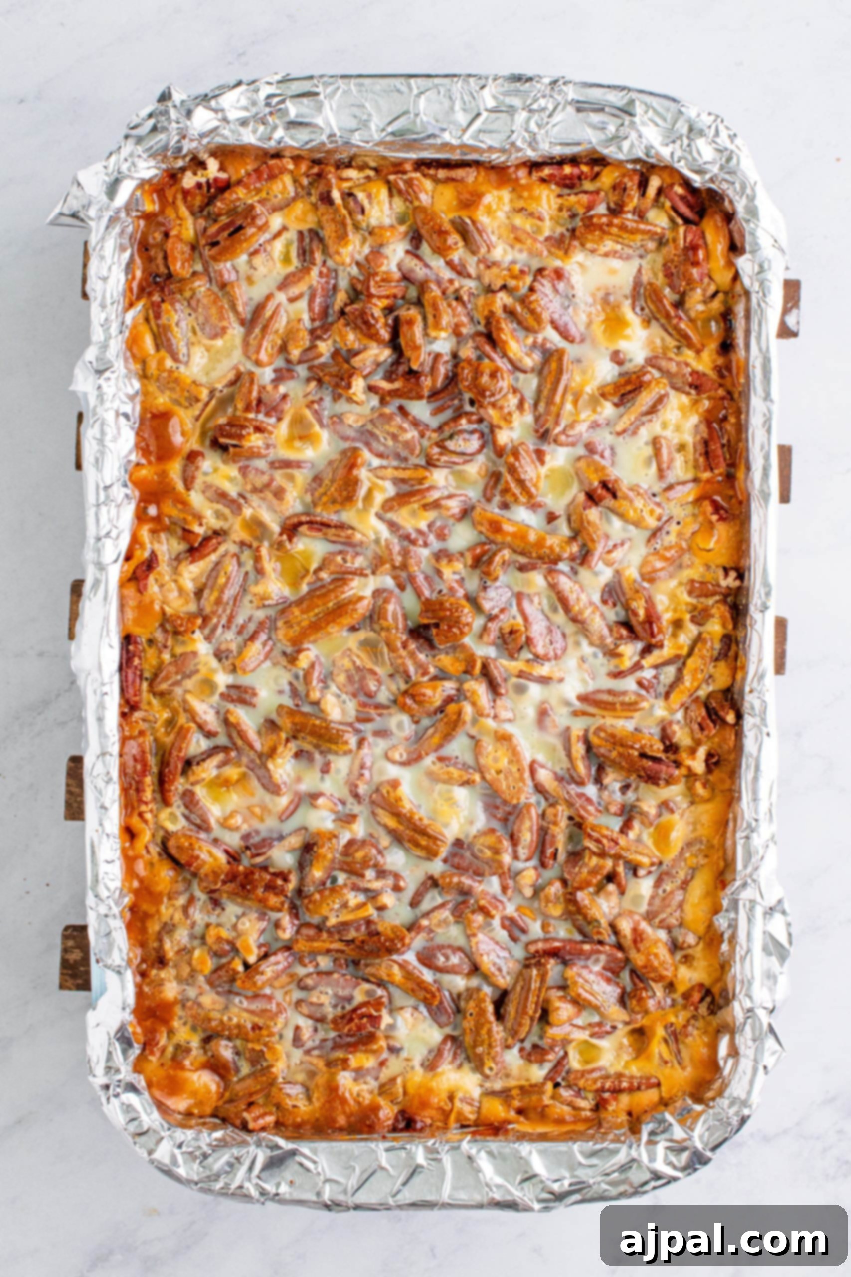 Baked pumpkin magic bars topped with golden pecans in a cookie sheet, cooling after baking