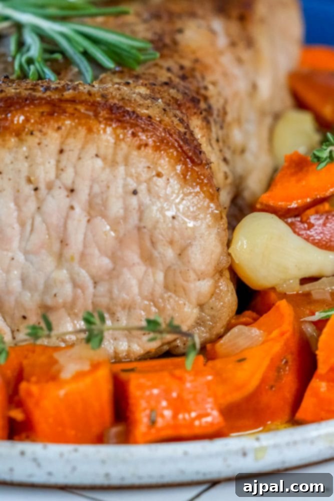 A beautifully roasted pork loin served alongside golden sweet potatoes, garlic cloves, and fresh herbs on an elegant plate.