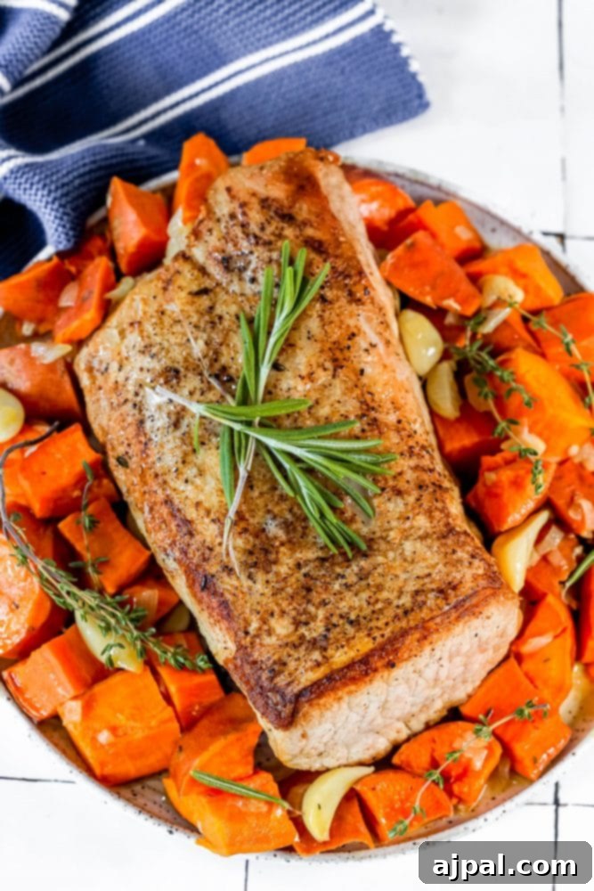 A hearty plate featuring roasted pork loin, golden sweet potatoes, and vibrant green herbs, ready for serving.