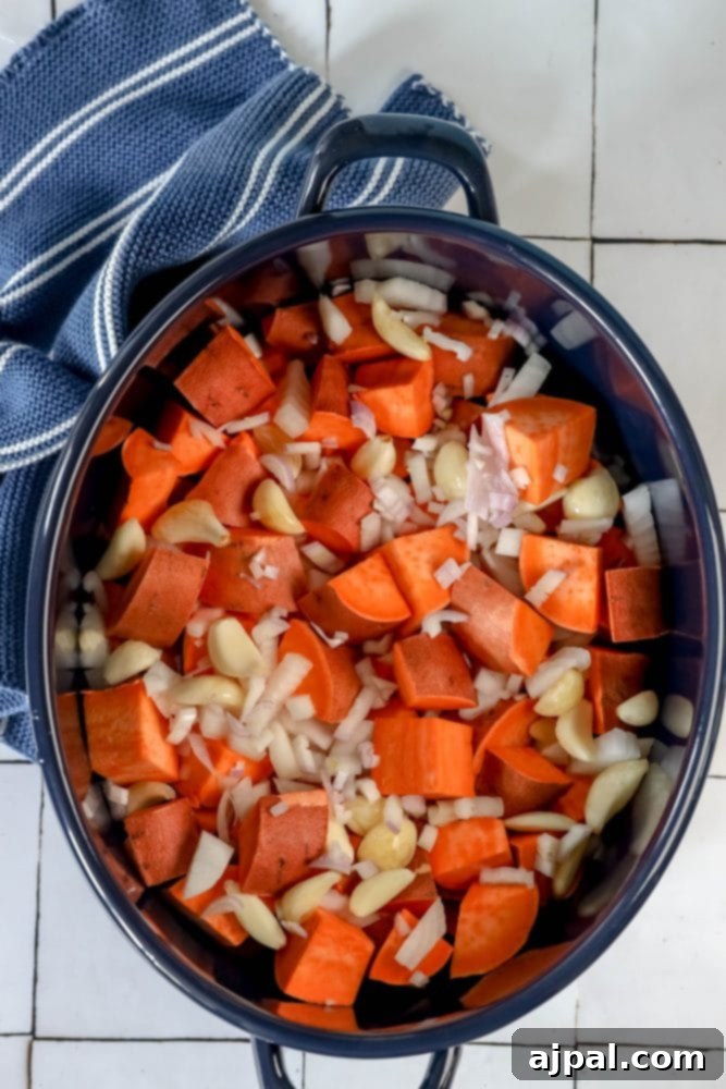 Freshly cut sweet potatoes, garlic, and herbs spread on a baking sheet, ready for the oven.