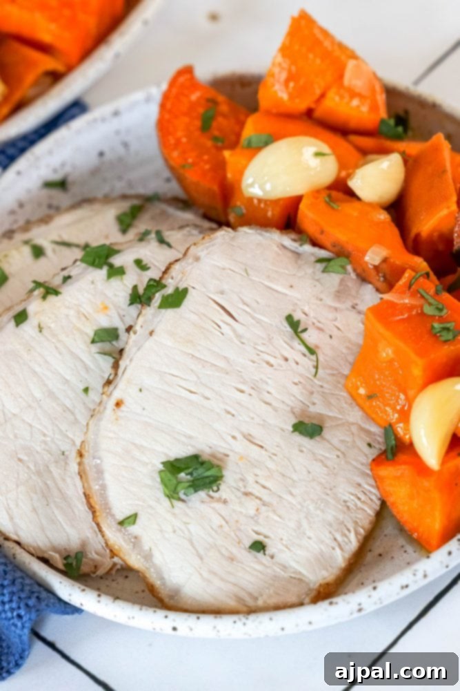 A beautifully presented serving of roasted pork loin and sweet potatoes, garnished with fresh herbs, on a wooden board.
