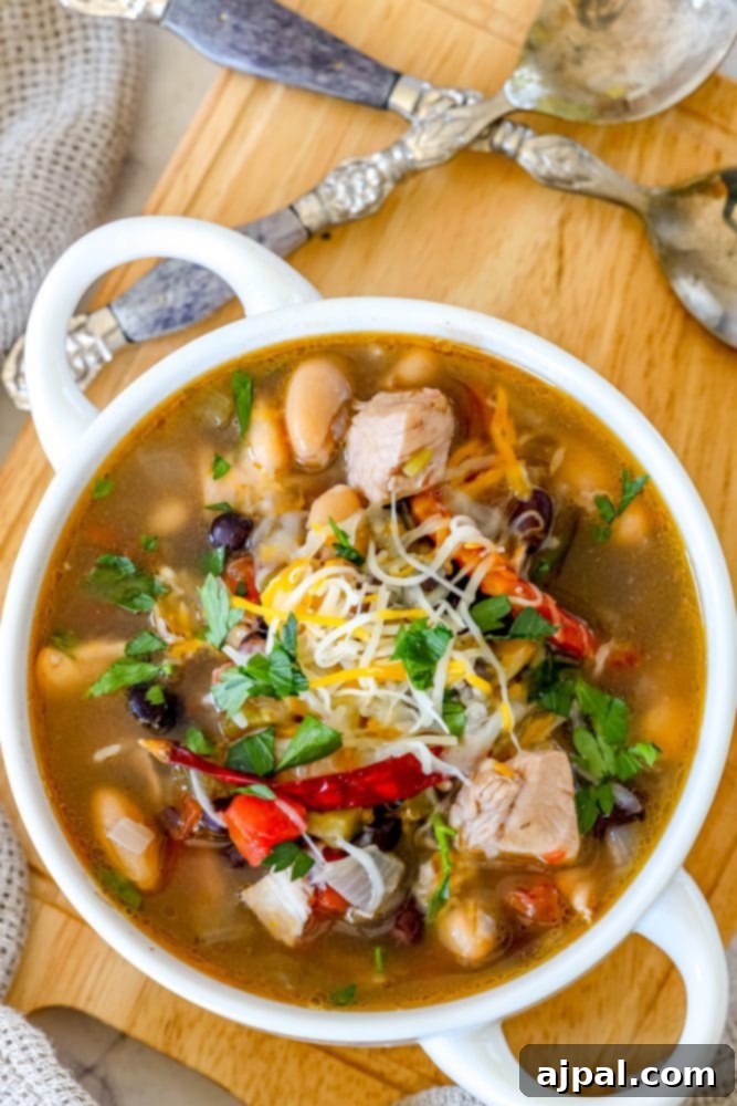 Close-up of a white bowl overflowing with savory Green Chile Chicken Soup, featuring visible chunks of chicken, colorful peppers, and beans, ready to be enjoyed.