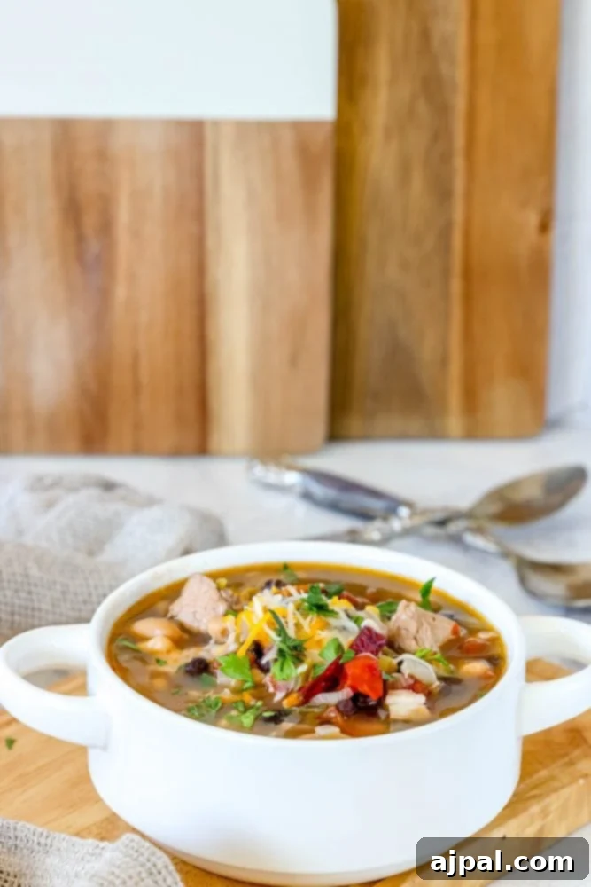 A beautifully presented bowl of spicy Green Chile Chicken Soup, richly garnished with cheese and cilantro, sitting on a rustic wooden board, inviting a hearty meal.