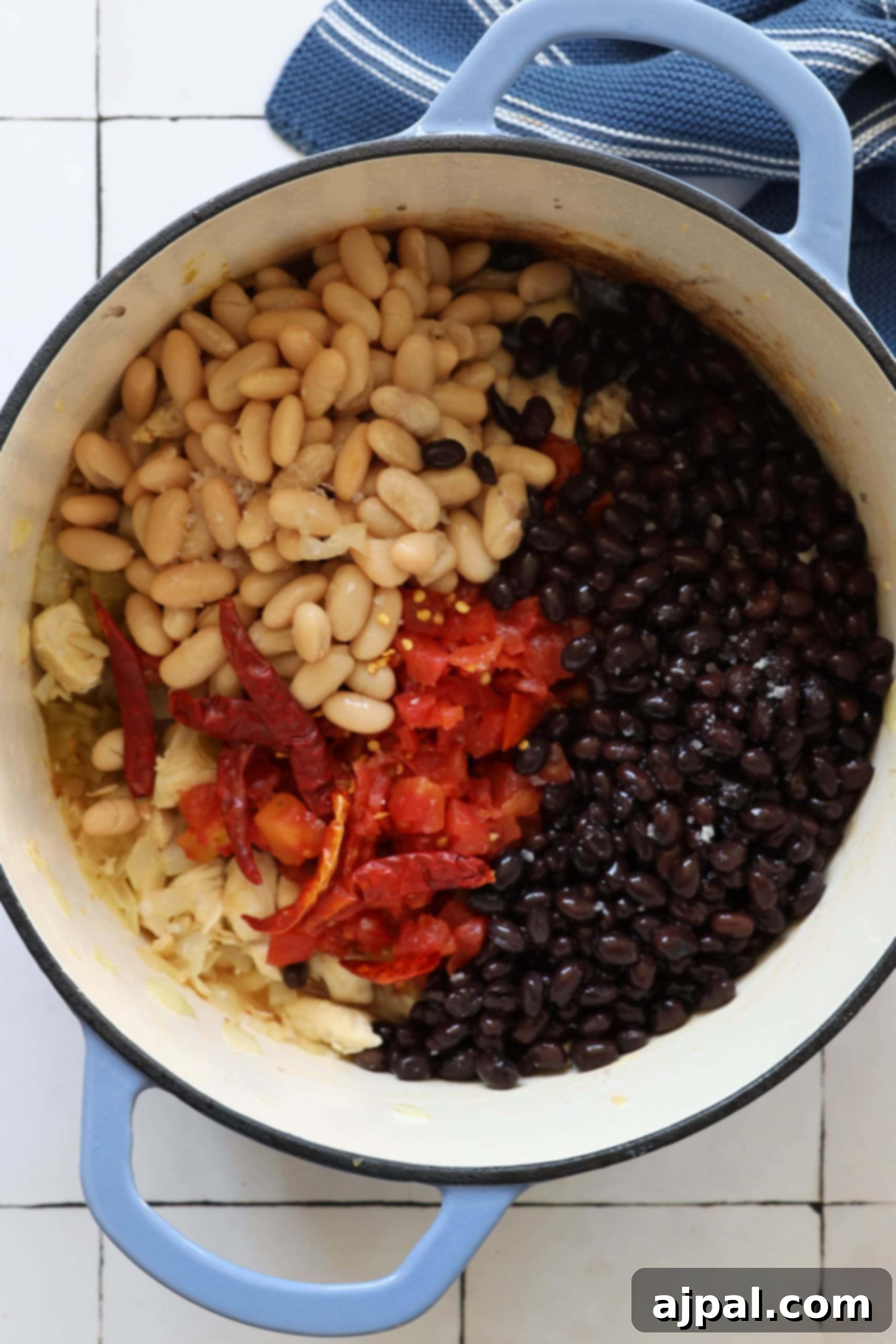 Hearty Green Chile Chicken Soup with diced chicken, Rotel tomatoes, green chilies, a mix of beans, and whole dried chilies, simmering gently in a Dutch oven to deepen its rich flavors.