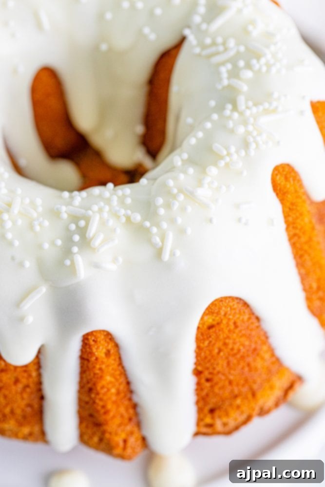 Perfect Air Fryer Pumpkin Bundt Cake 4 A festive air fryer pumpkin bundt cake, elegantly decorated with icing and colorful sprinkles, sits on a white cake stand.
