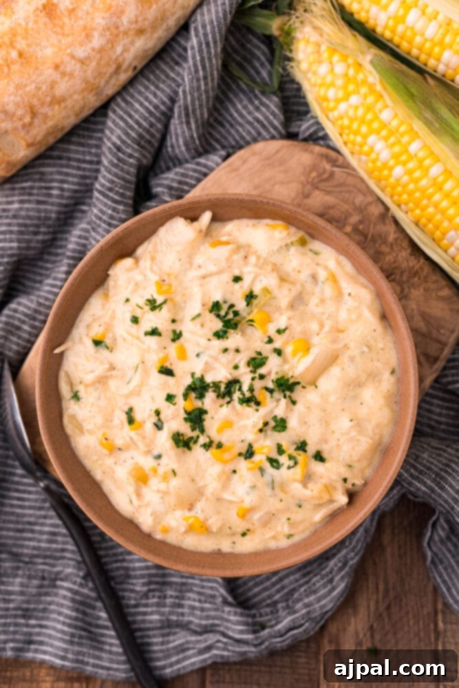 Creamy Corn Chowder 12 A rustic bowl of creamy corn chowder with shredded chicken and a sprig of parsley, served with a side of crusty bread.