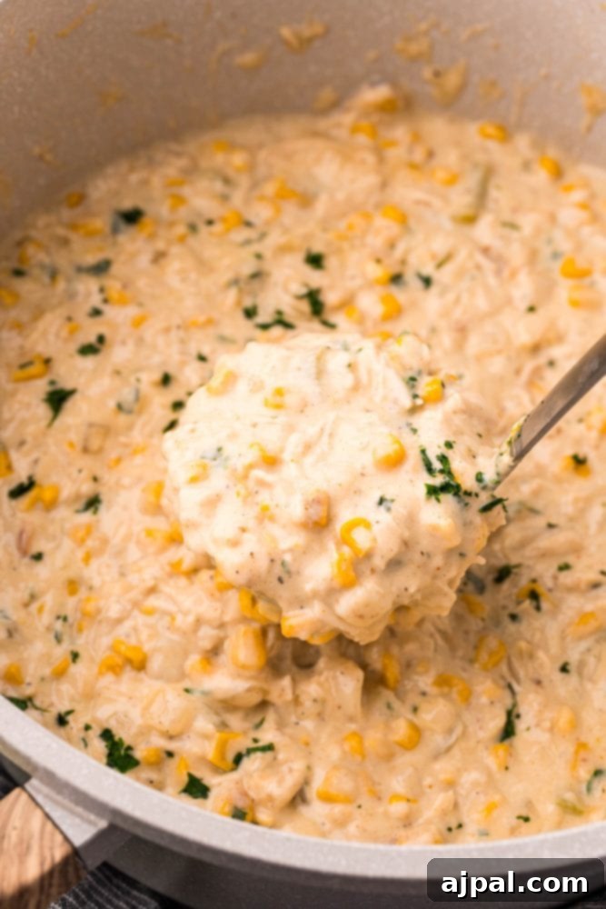Creamy Corn Chowder 4 A spoon lifts a generous scoop of rich, creamy corn chowder from a large pot, showing off its thick texture and wholesome ingredients.