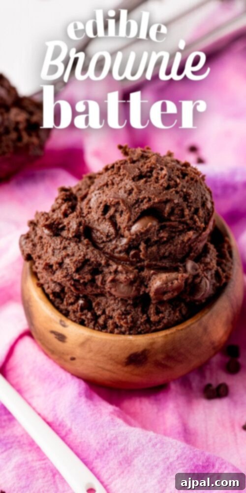 No-Bake Brownie Batter 14 A beautifully styled wooden bowl filled with rich, fudgy edible brownie batter, with a serving spoon resting inside, presented on a soft pink background. This no-bake dessert is perfect for chocolate lovers.