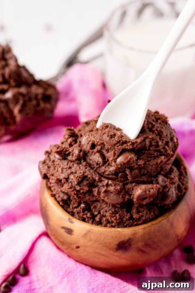No-Bake Brownie Batter 10 A wooden bowl filled with rich, fudgy edible brownie batter, with a spoon resting in it, ready to be enjoyed. The bowl is set on a light background.