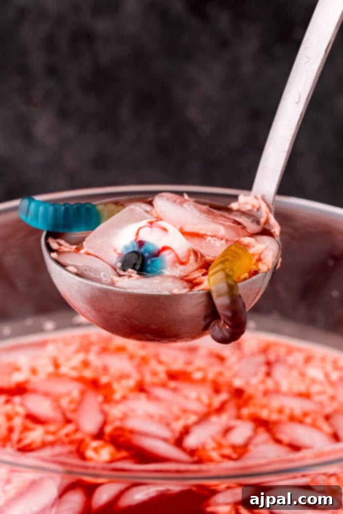 A spoon lifting a portion of sparkling Halloween fruit punch, revealing gummy worms submerged in the delightful drink.