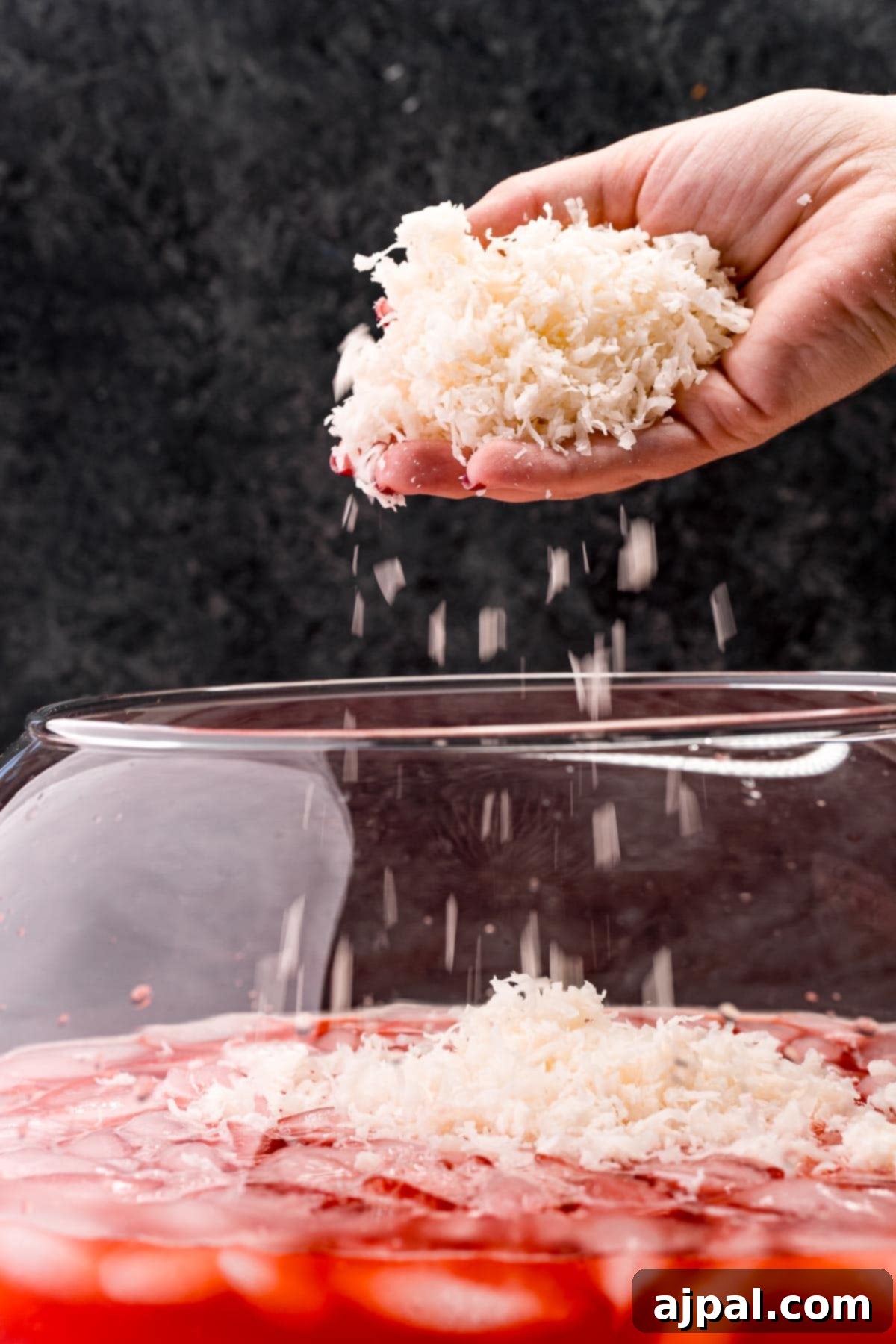 Shredded coconut being sprinkled onto the surface of the punch, creating a frothy, web-like texture.