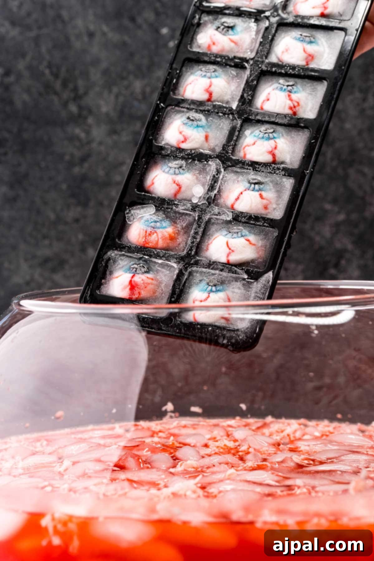 Gummy eyeball ice cubes being gently added to the punch for a final spooky touch.