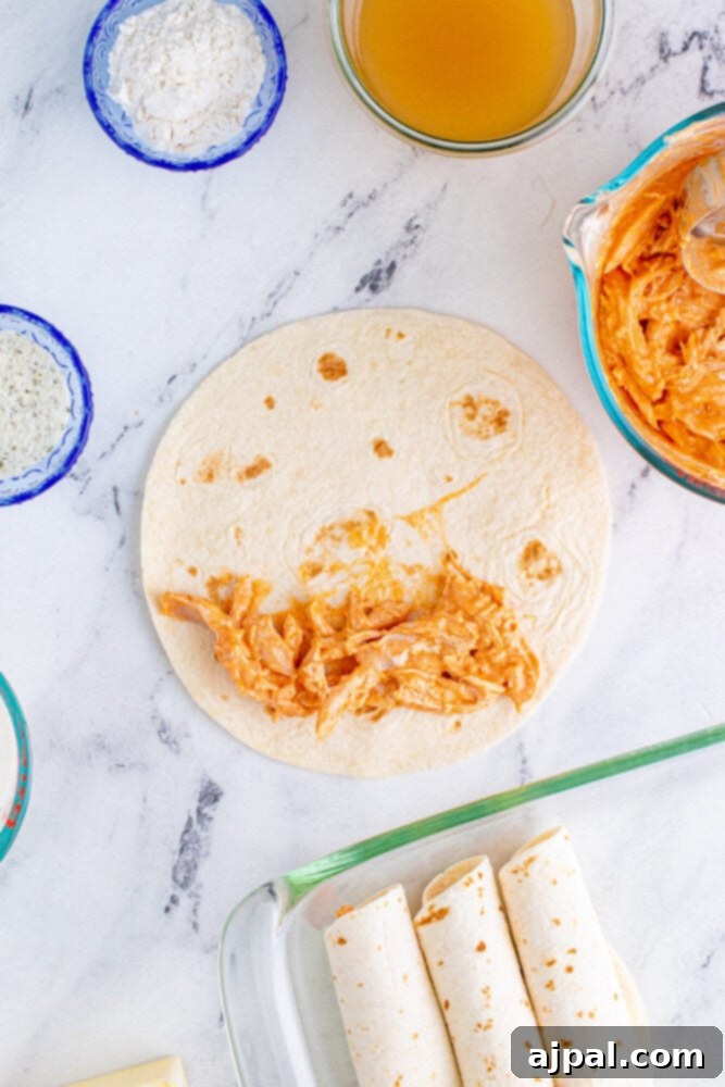 Shredded chicken generously coated in buffalo sauce and sour cream, next to a stack of tortillas, ready for assembly.