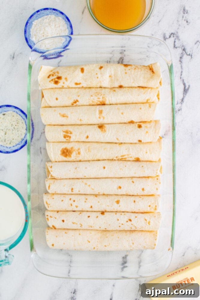 Carefully rolled enchiladas, filled with buffalo chicken mixture, neatly arranged seam-side down in a baking dish.