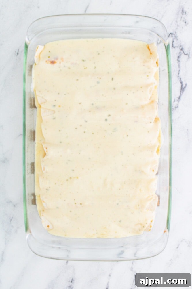 Enchiladas in a baking dish, thoroughly covered with the rich, creamy ranch sauce.