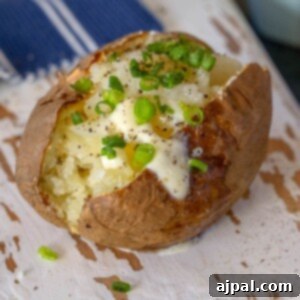 picture of baked potato with a pat of butter and chives on a wood cutting board