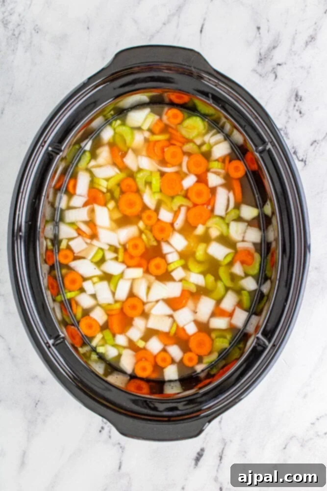 Chicken, vegetables, and chicken stock filling a slow cooker, illustrating the initial setup before slow cooking begins.