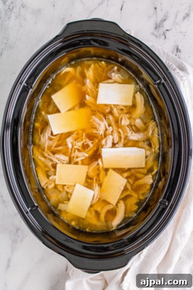 Shredded chicken, fluffy dumplings, and a rich broth simmering together in a slow cooker, indicating the final stage of cooking.