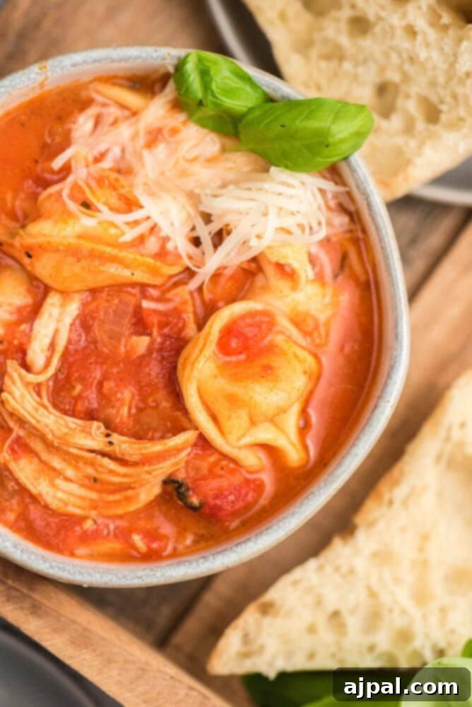 A bowl of chicken and tomato soup with bread on a wooden table.