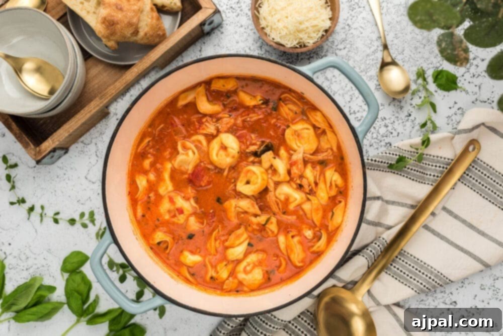 A pot of Tomato Basil Chicken Tortellini Soup with bread on a table.