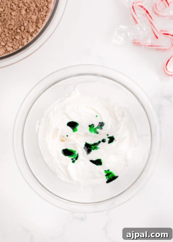 Festive Fudgy Evergreen Brownies 14 Drops of vibrant green food coloring being added to smooth white frosting in a bowl, preparing for mixing.
