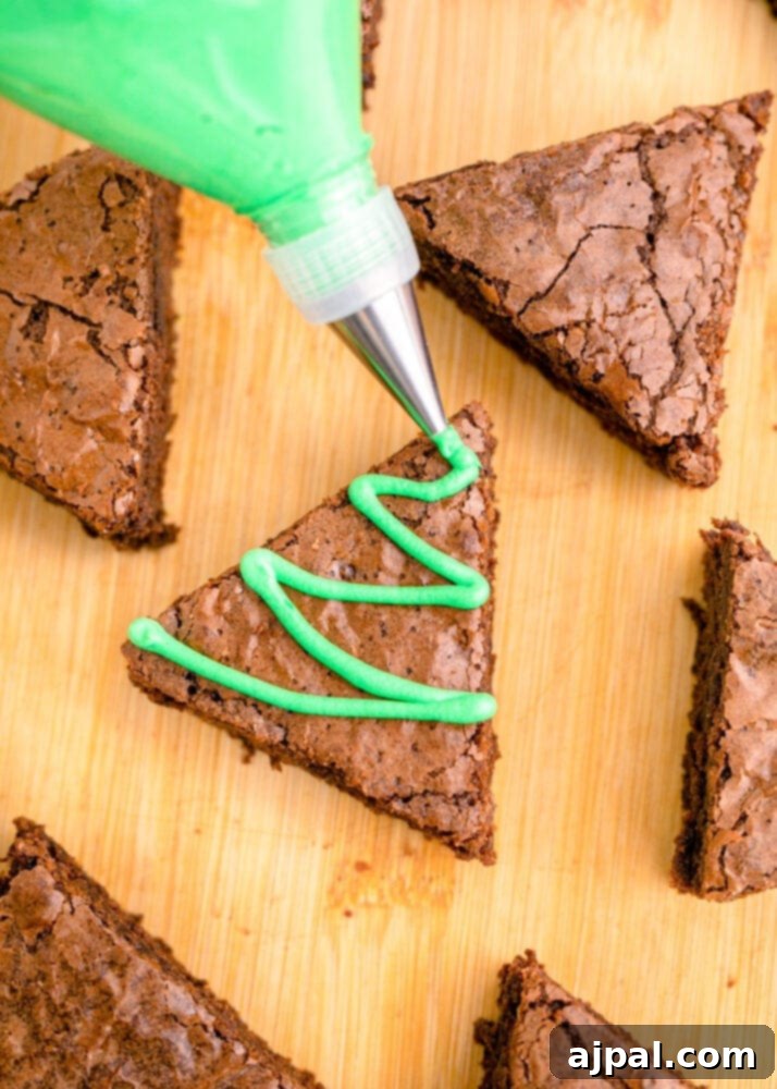 Festive Fudgy Evergreen Brownies 17 Green frosting being piped onto a triangle brownie in a zig-zag pattern, beginning to create the Christmas tree effect.