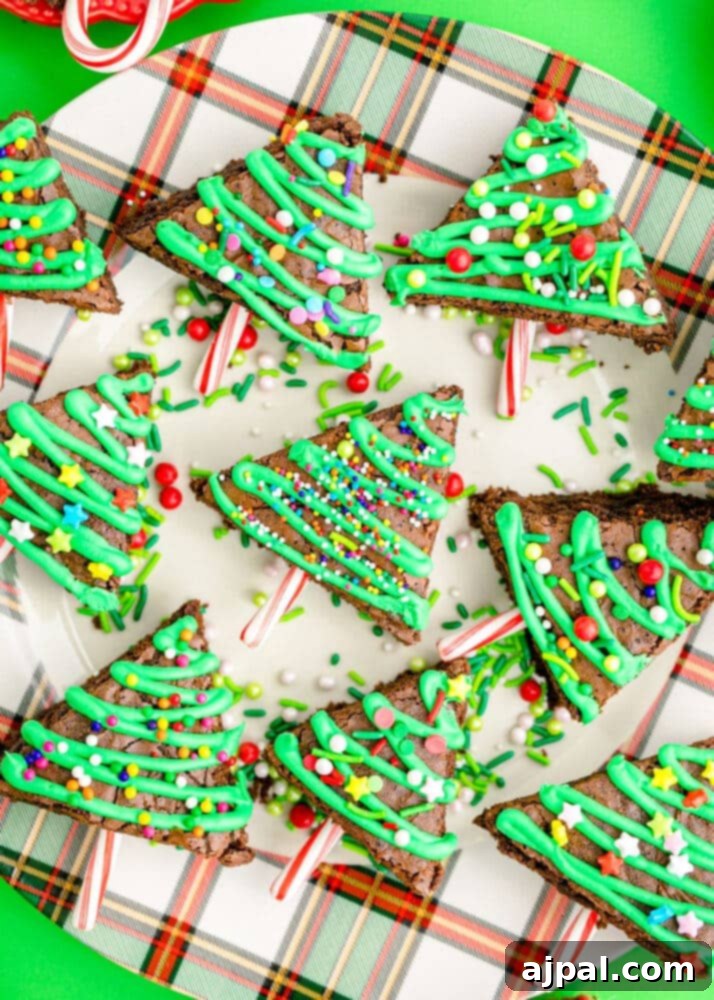 Festive Fudgy Evergreen Brownies 20 A festive Christmas tree brownie topped with green icing, colorful sprinkles, and a candy cane trunk, resting on a plate.