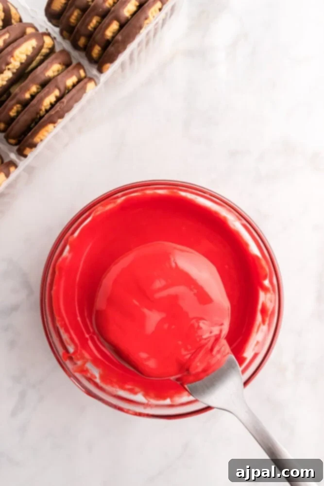 Effortless Christmas Wreath Cookies 7 A vibrant bowl of rich red icing, with a spoon poised, surrounded by an array of festive Christmas wreath cookies awaiting their decorative finish.