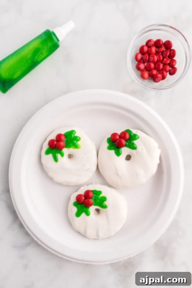 Effortless Christmas Wreath Cookies 9 A pristine white Christmas wreath cookie artfully decorated with vibrant green holly leaves and three glistening red M&M berries.