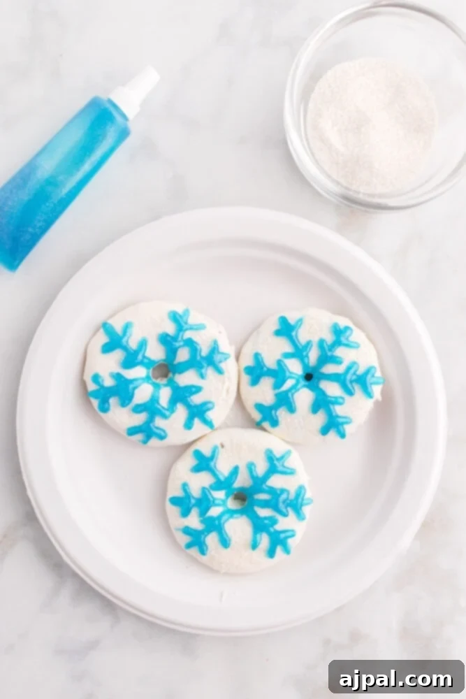 Effortless Christmas Wreath Cookies 10 An enchanting white Christmas wreath cookie adorned with shimmering silver sanding sugar and a delicate blue icing snowflake design.