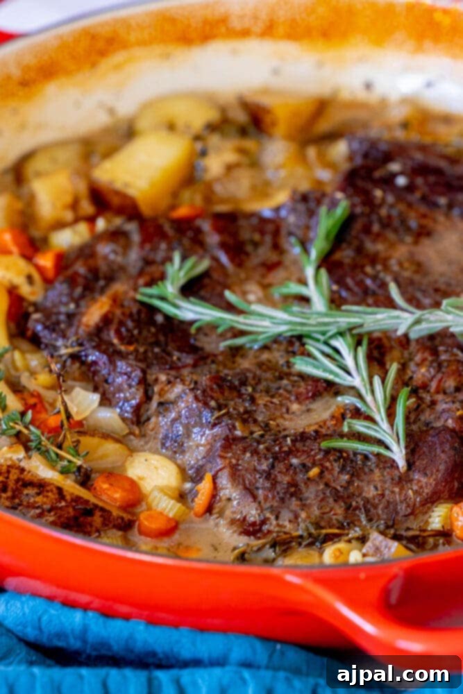 Ultimate Comfort Pot Roast with Tender Potatoes 2 A perfectly cooked pot roast in a Dutch oven with vegetables and rosemary sprigs on top.