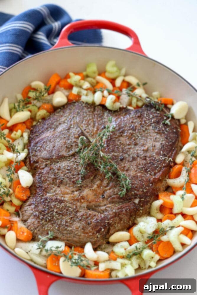 Ultimate Comfort Pot Roast with Tender Potatoes 9 A browned pot roast in a pan, surrounded by potatoes, carrots, and thyme sprigs.