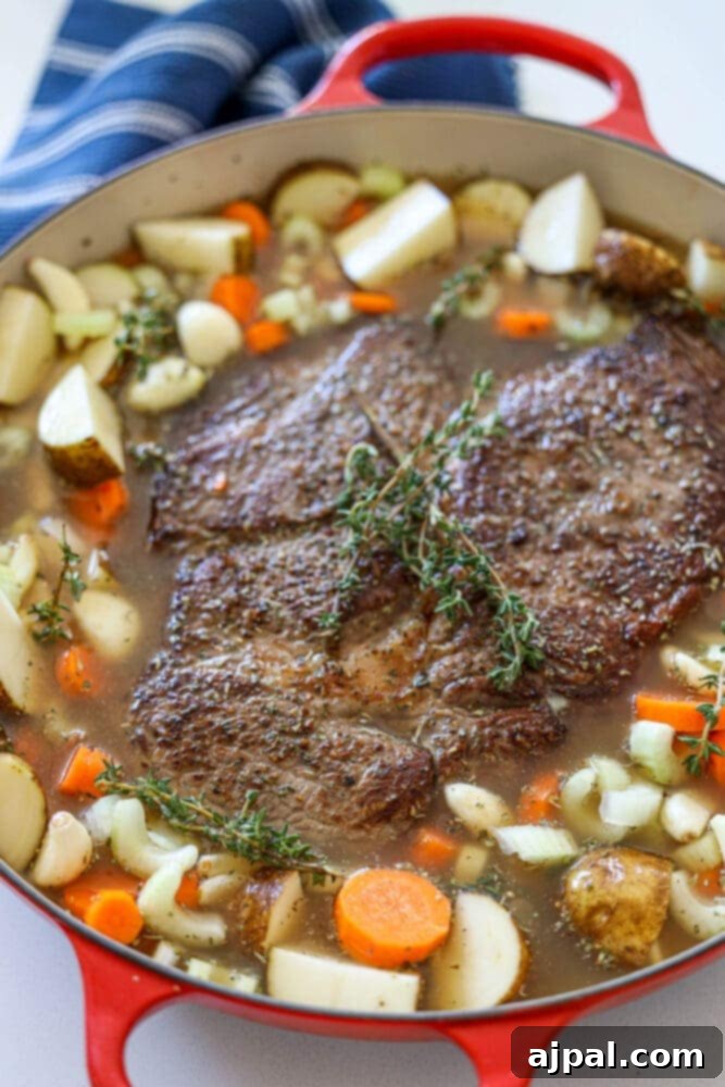 Ultimate Comfort Pot Roast with Tender Potatoes 10 A browned pot roast simmering in a Dutch oven with beef stock and mixed vegetables.