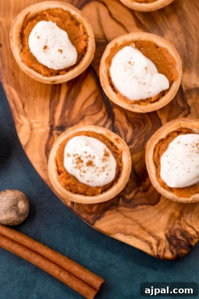 Perfectly baked mini sweet potato pies, each crowned with a swirl of whipped cream and a dash of cinnamon, presented on a rustic wooden cutting board.