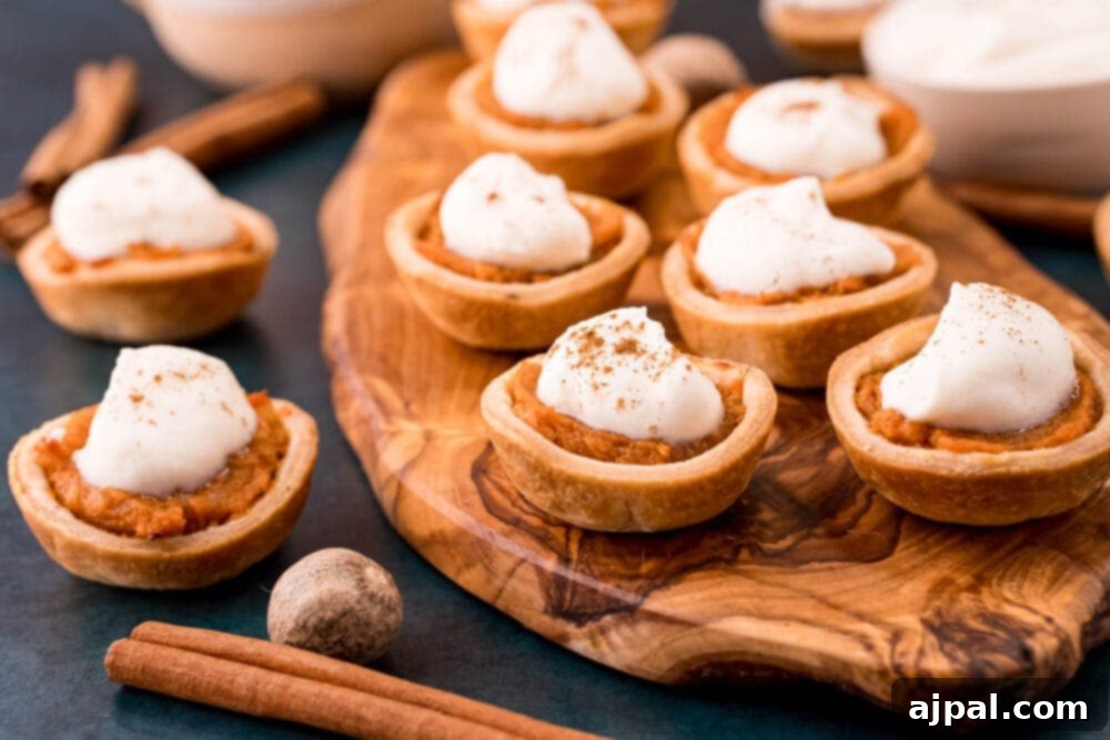 Three mini sweet potato pies, each adorned with whipped cream and a sprinkle of cinnamon, rest on a rustic wooden cutting board, inviting a delightful experience.