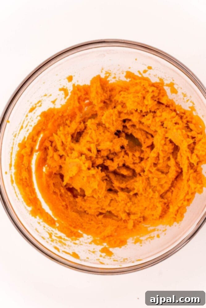 A close-up of fluffy, mashed sweet potatoes in a white mixing bowl, ready to be transformed into a delicious pie filling.