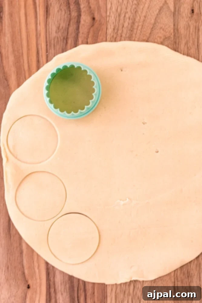 Rolled-out pie dough on a floured surface, neatly cut into perfect circles with a biscuit cutter, ready for shaping into mini pie crusts.