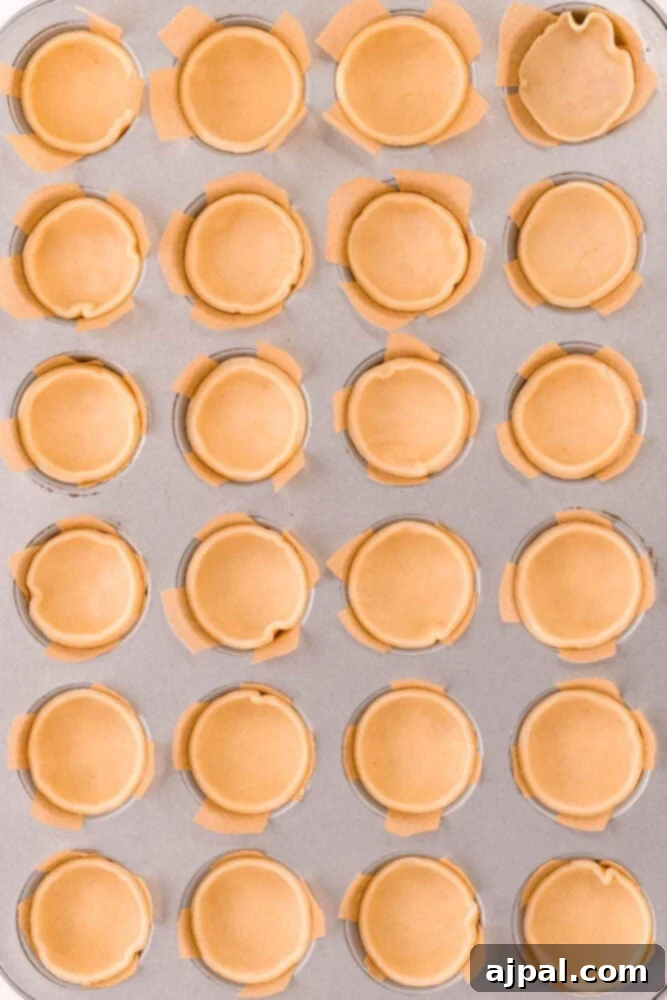 Mini pie dough circles meticulously pressed into individual cavities of a mini muffin tin, creating perfect cups ready for filling.