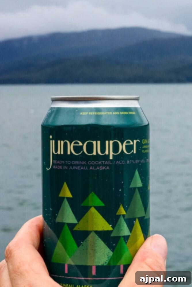 A person proudly holding a can of Juneauper, a local craft beverage, with the scenic backdrop of Juneau, Alaska's natural beauty.