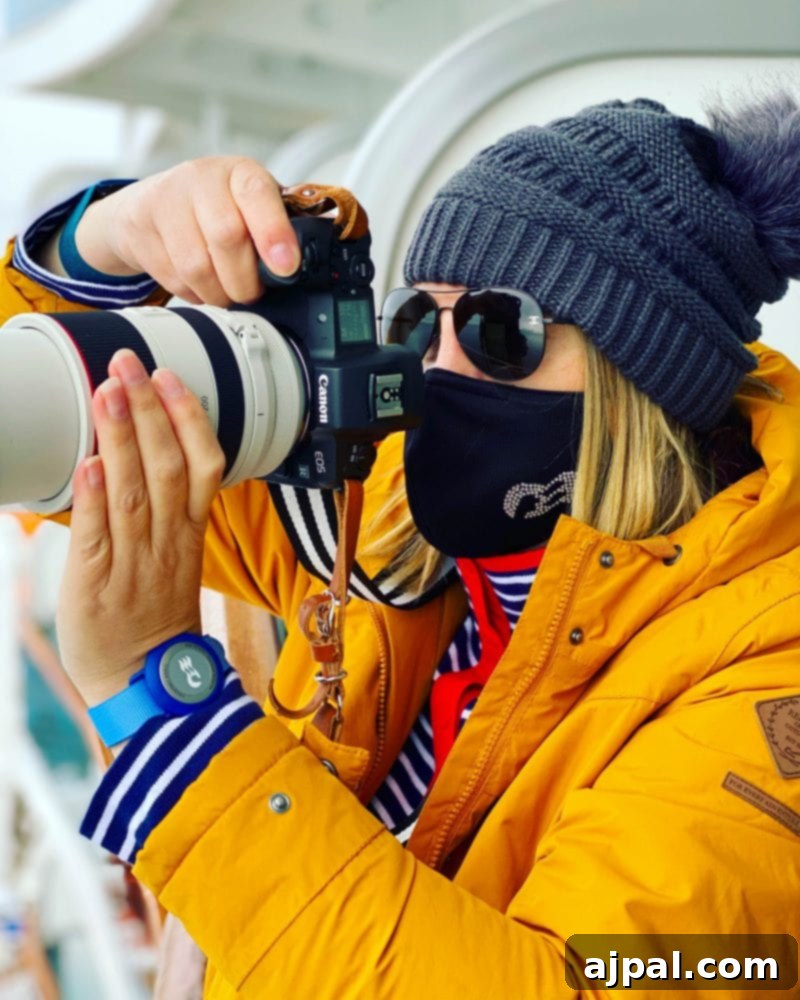 A woman in a vibrant yellow jacket and face mask, capturing the scenic beauty of Alaska from the deck of the Majestic Princess cruise ship.