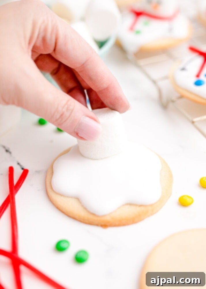 Snowman Meltdown Cookies 20 picture of a hand putting a marshmallow on a cookie with wet icing, forming the snowman's head