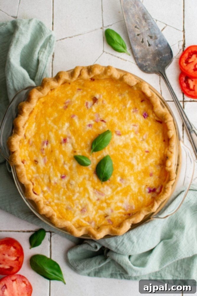 Simple Savory Tomato Pie 3 A whole baked tomato pie, golden brown with bubbly cheese, sitting on a charming tiled surface.