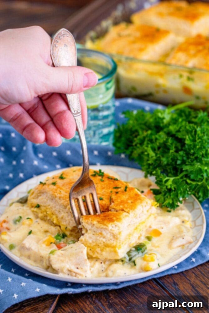 A slice of turkey pot pie on a white plate, with a fork cutting into the golden-brown crust.
