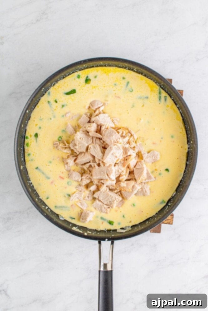 Cooked turkey pieces gently folded into the pot pie filling, ensuring every piece is coated in the rich sauce.