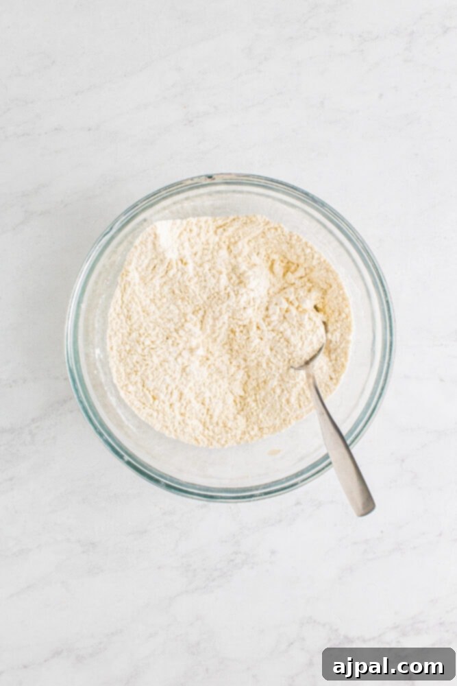 A bowl containing all-purpose flour, baking powder, sugar, salt, and baking soda, waiting to be mixed for the biscuit topping.